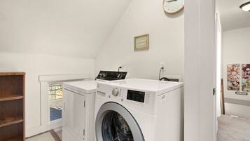 A laundry room with two washing machines, a wooden shelf, a clock, and a small window.