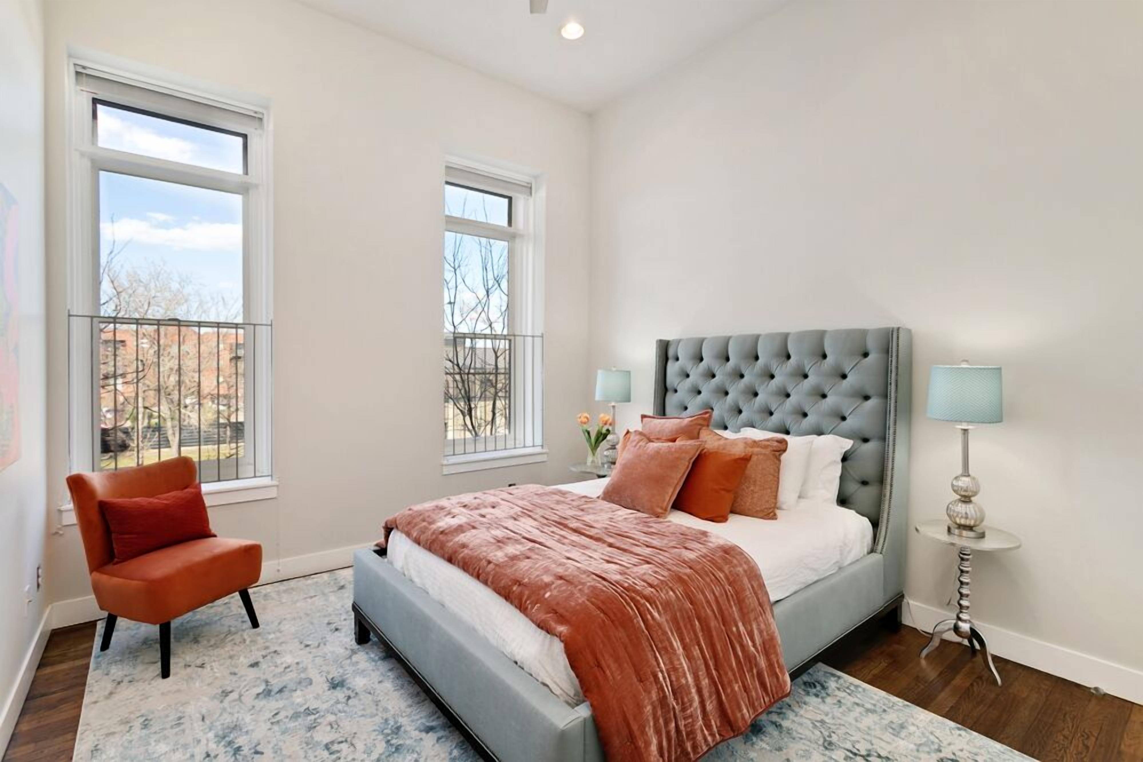 Un dormitorio con una cama grande, dos ventanas, una silla y una lámpara.