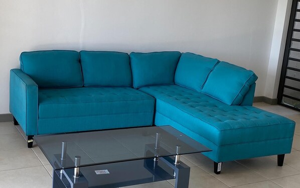 A teal sectional sofa with a glass coffee table in front.