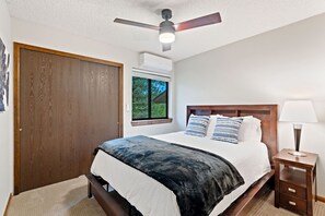 Un dormitorio con cama, ventilador de techo, ventana y mesita de noche.