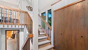 Una escalera de madera con peldaños alfombrados que conduce a una plataforma, una puerta de madera grande y vistas de la montaña a través de una ventana.