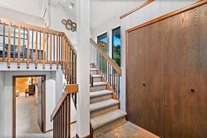 A wooden staircase with carpeted steps leading to a landing, a large wooden door, and a view of a mountain through a window.