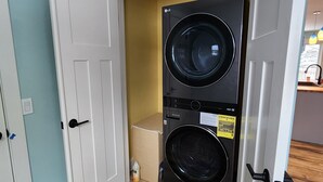 A laundry room with two stacked front-loading washers and dryers, wooden flooring, and a white door. - Cozy Lake and Mountain View House (Somers)