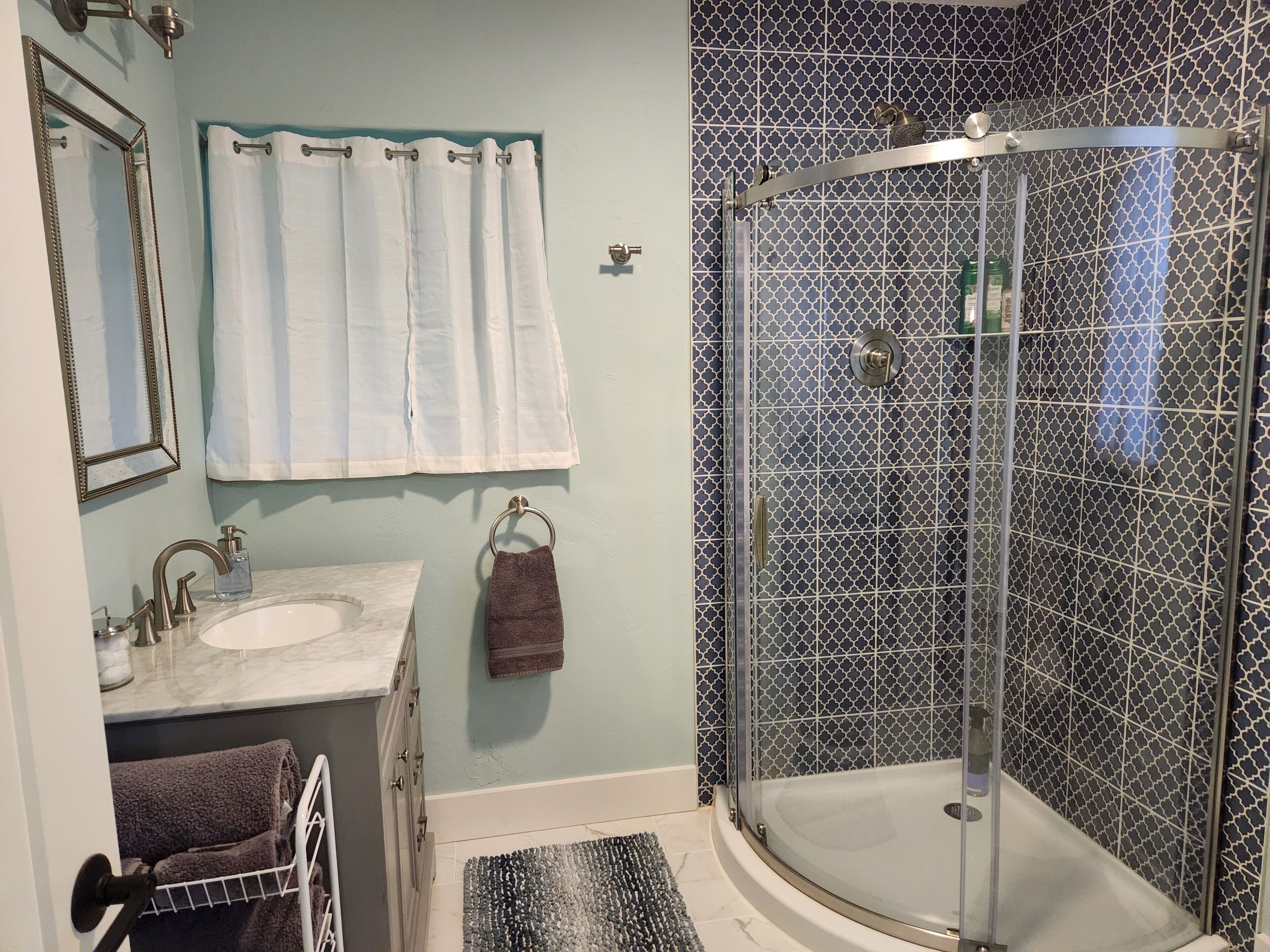 A bathroom with a glass-enclosed shower, a sink with a marble countertop, and a towel rack with towels.