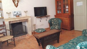 A living room with a fireplace, a television, a cabinet, and patterned furniture. - Gîte Les Glycines, Sologne getaway, nature & relaxation 10 min from Chambord (Crouy-sur-Cosson)