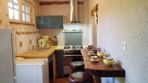 A compact kitchen with a stove, sink, and a small refrigerator. There are stools and a wooden table with yellow teapots. - Gîte Les Glycines, Sologne getaway, nature & relaxation 10 min from Chambord (Crouy-sur-Cosson)