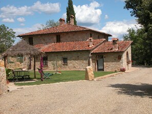A stone building with a tiled roof, a thatched-roof structure, and a gravel driveway. - Farmhouse with beautiful pool and jacuzzi, panoramic location in chianti (castellina in chianti)