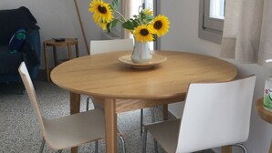Ein runder Holztisch mit weißen Stühlen, eine Vase mit Sonnenblumen und eine Lampe auf einem Beistelltisch.