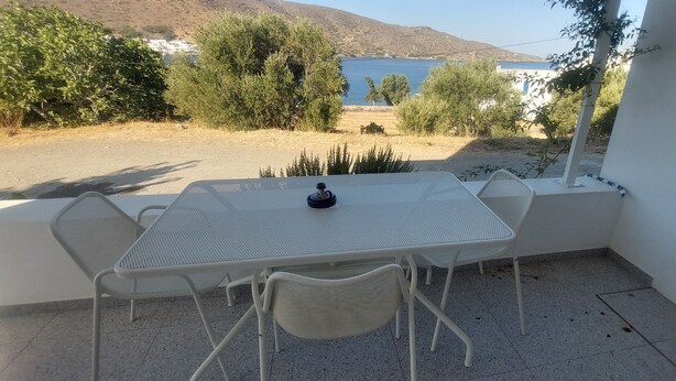 Eine Terrasse mit Tisch und Stühlen, mit Blick auf ein Gewässer und Hügel.