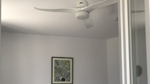 Ein Schlafzimmer mit einem Bett, zwei Nachttischen, einem Deckenventilator und einem gerahmten Kunstwerk an der Wand.