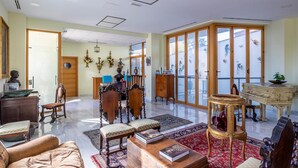 Ein geräumiges Wohnzimmer mit großem Fenster, einem Klavier und verschiedenen Möbelstücken, darunter eine Couch, Sessel und ein Couchtisch.