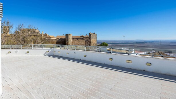 Eine Dachterrasse mit freiem Blick auf ein historisches Steinhaus und die ferne Landschaft.