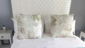 Una cama con cabecera blanca, dos almohadas estampadas con motivos florales y una manta color turquesa.