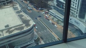 Vista desde un edificio alto con vistas a un paisaje urbano que incluye edificios modernos, una calle concurrida y un estacionamiento.