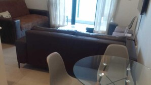 Un espacio habitable compacto con una mesa de comedor de vidrio, dos sillas, un sofá y un televisor montado en la pared.