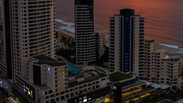 Un paisaje urbano costero con rascacielos, incluyendo una estructura curva distintiva, y vista del océano al atardecer.