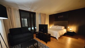 Una camera d'albergo moderna con divano, televisore, comodino e un letto con testiera.