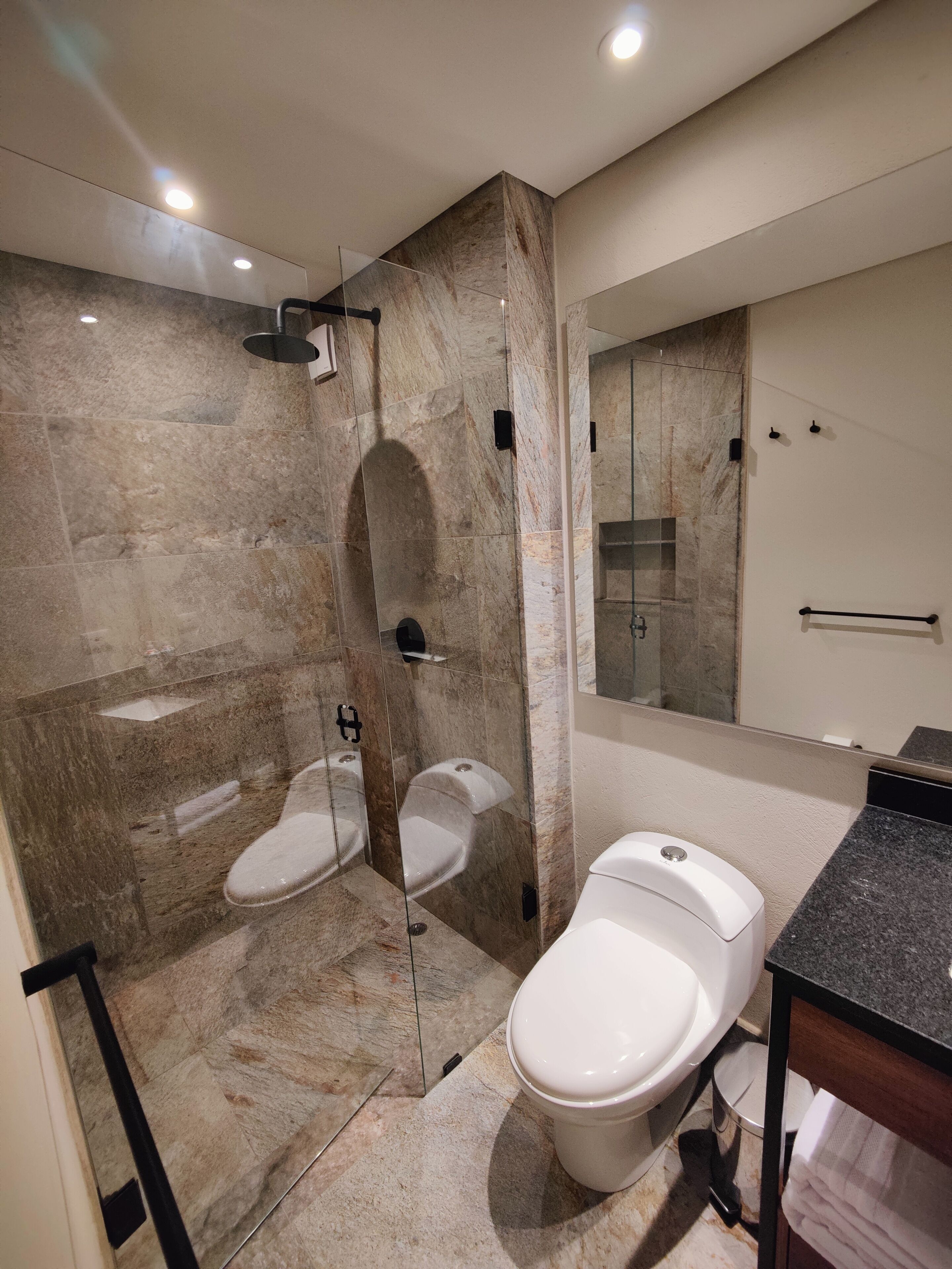 Een moderne badkamer met een douche, twee toiletten, een wastafel en een grote spiegel.