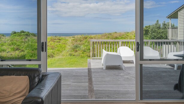 Et moderne værelse med en stor skydedør til en balkon med hvide stole og havudsigt.