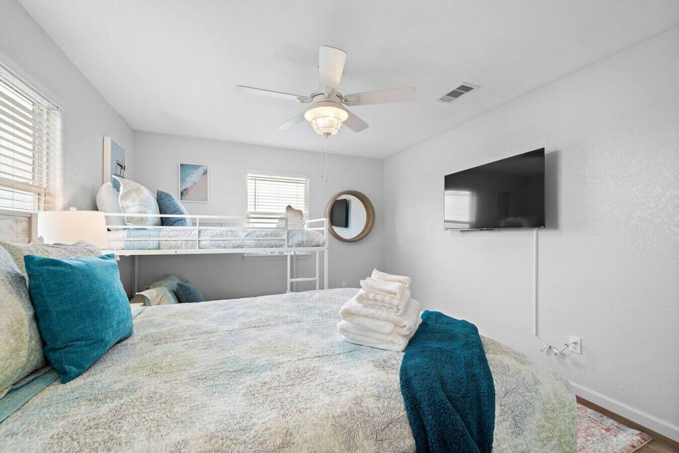 A bedroom with bunk beds, a ceiling fan, a TV, and a window with blinds.