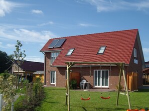 A two-story house with a red-tiled roof, solar panels, and a swing set in the front yard.