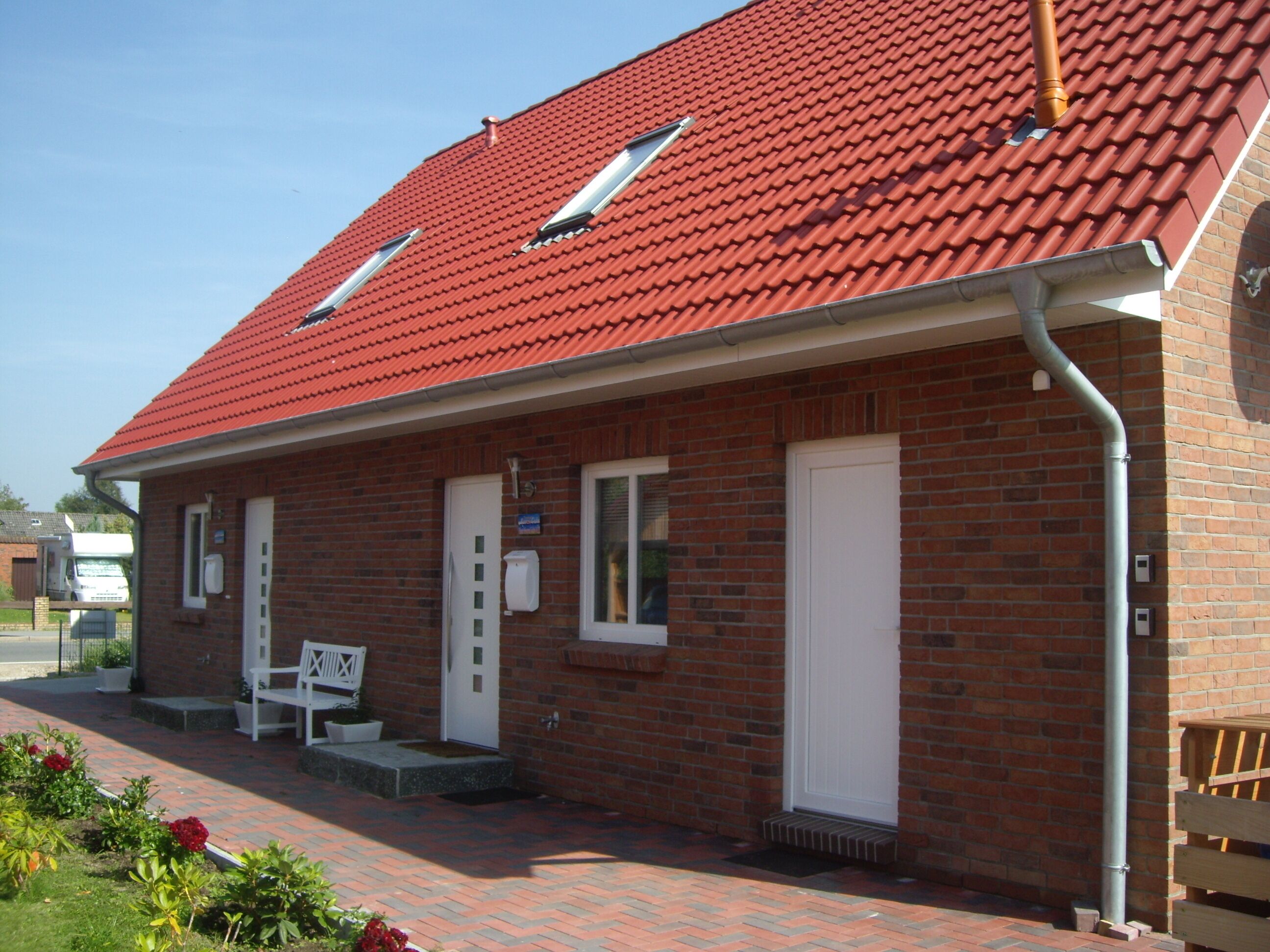 Ein Backsteinhaus mit rotem Ziegeldach, einer weißen Tür und einer kleinen Veranda mit einer Bank.