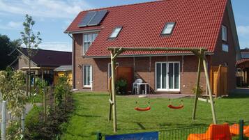 Ein zweistöckiges Haus mit rotem Ziegeldach, einem eingezäunten Garten und einer Schaukel.