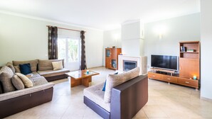 A modern living room with a sectional sofa, a coffee table, a flat-screen TV, and a fireplace. - Relaxing stay w/ heatable pool & BBQ (Albufeira)