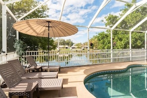 A covered outdoor swimming pool with lounge chairs and an umbrella.