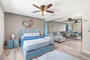 Une chambre à coucher comprenant un lit, une table de chevet, une commode, un ventilateur de plafond et un miroir.