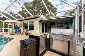 An outdoor kitchen area with a grill, a sink, and a poolside setting.