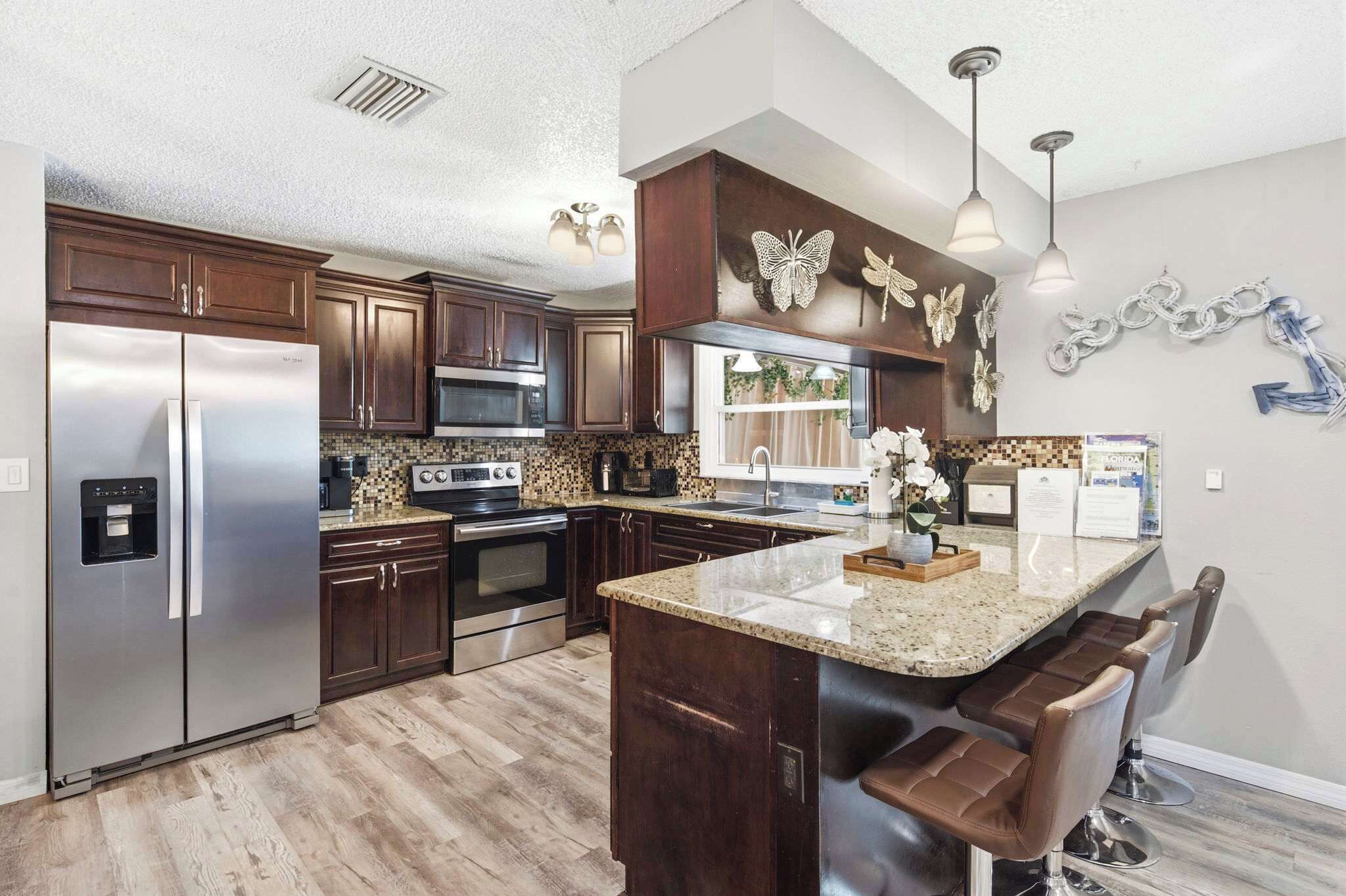A modern kitchen with stainless steel appliances, dark wood cabinets, a granite countertop, and decorative wall art.