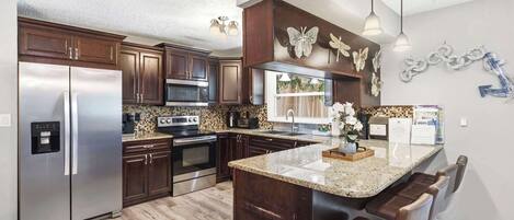 A modern kitchen with stainless steel appliances, dark wood cabinets, a granite countertop, and decorative wall art.