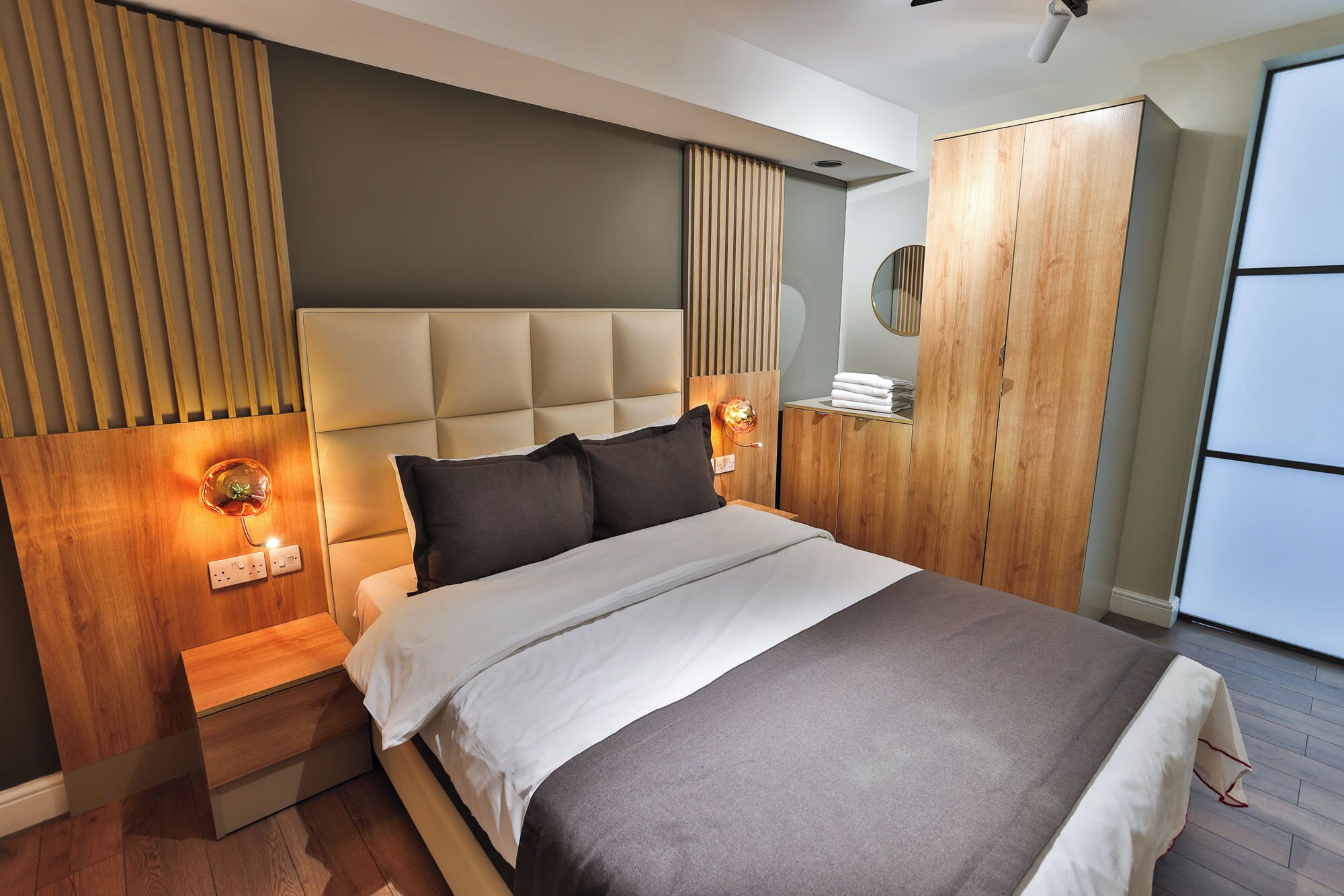 Un dormitorio moderno con una cama grande, cabecera de madera, lámparas de noche y un armario.