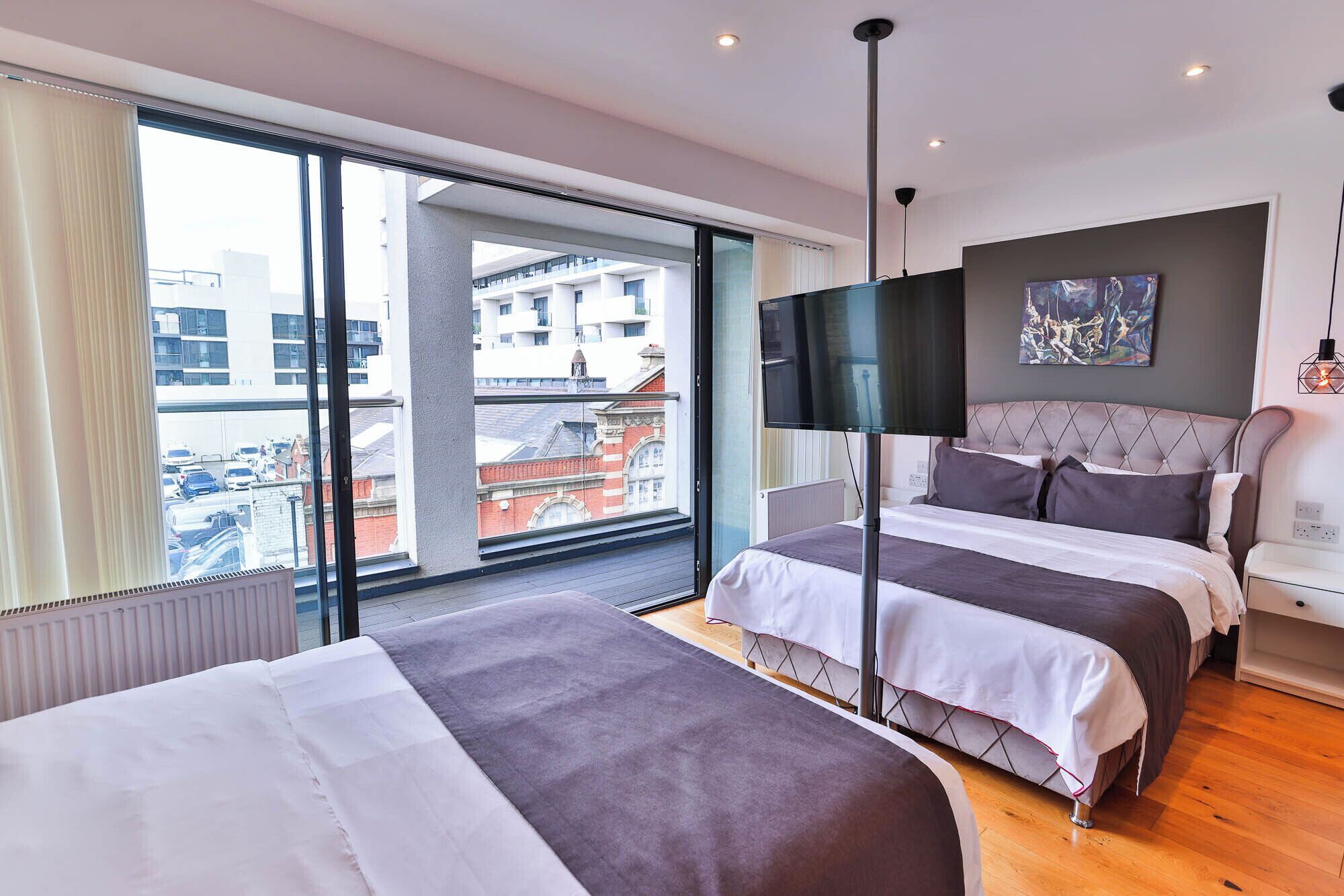 A modern hotel room with two beds, a large window with a view of buildings, a flat-screen TV, and a painting on the wall.