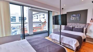 A modern hotel room with two beds, a large window with a view of buildings, a flat-screen TV, and a painting on the wall.