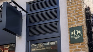 A building entrance with a black door, a green sign with '11 Goodwin', and a brick wall. - Goodwin (London)