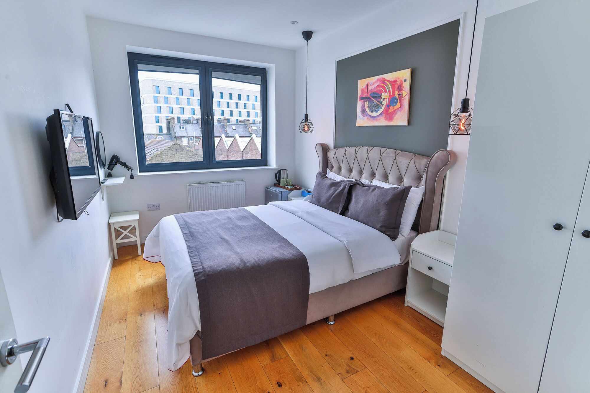 Une chambre moderne avec un lit, une table de chevet et une fenêtre donnant sur des immeubles.
