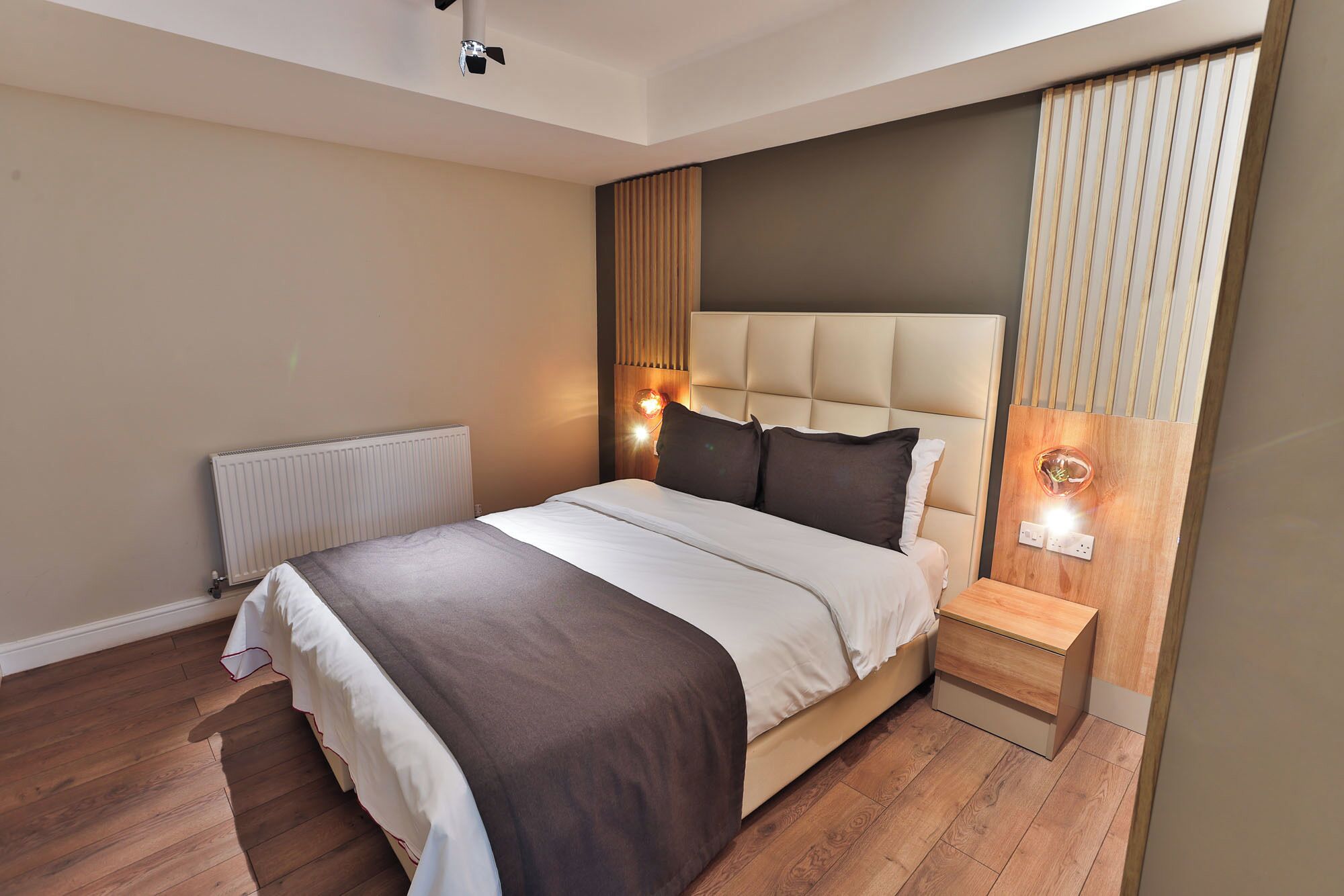 Un dormitorio moderno con una cama grande, una mesita de noche, una lámpara de pared y un radiador.