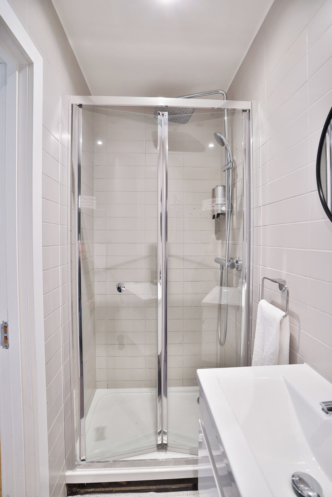 Un baño moderno con ducha envuelta en vidrio, un lavabo blanco y un espejo redondo.