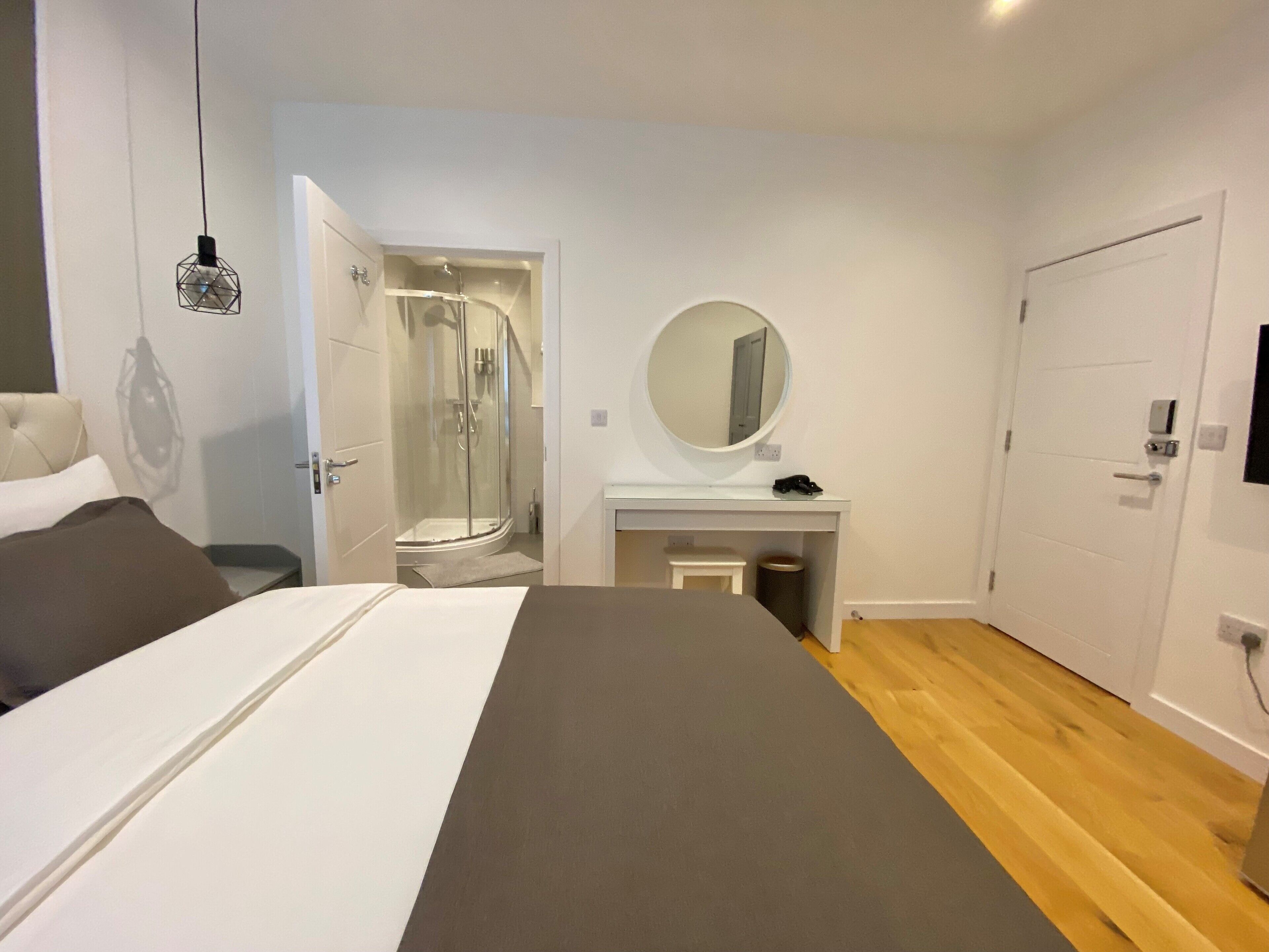Une chambre moderne comprenant un lit, un dressing, une salle de bain avec douche et une petite coiffeuse avec miroir.