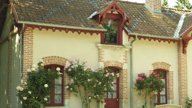Een traditioneel huis met een bakstenen gevel, meerdere ramen met decoratieve bogen en een pannendak.