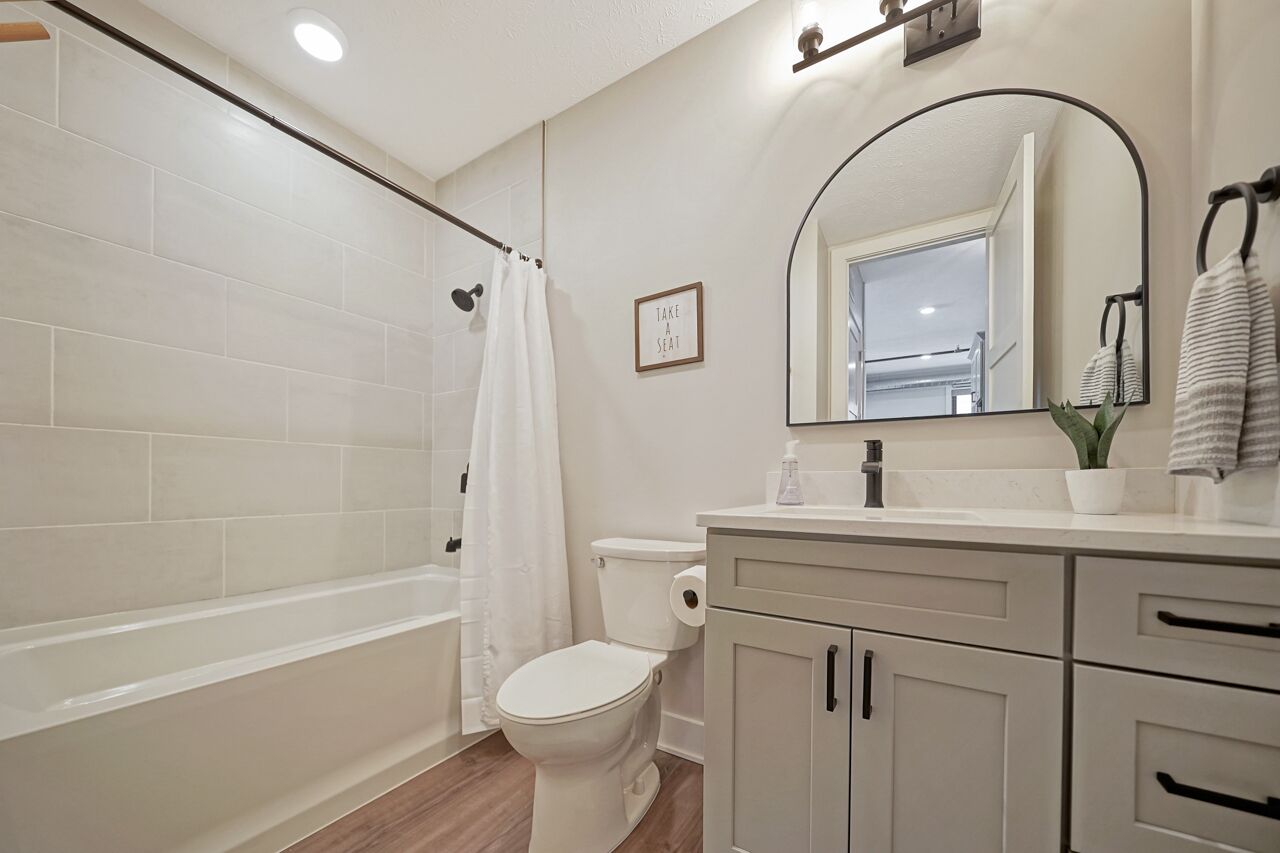 A bathroom with a bathtub, toilet, and vanity with a mirror.