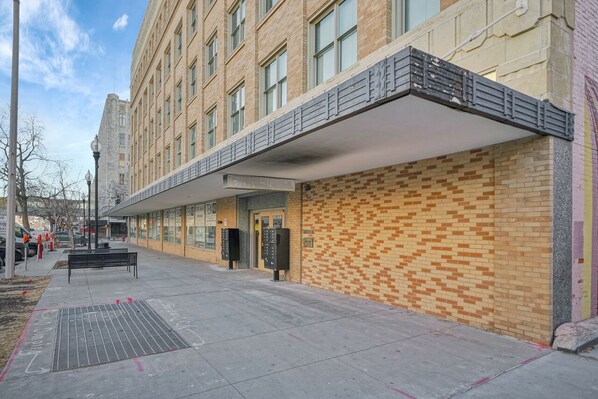 A building with a brick facade, a covered walkway, and a bench on the sidewalk.