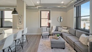 Een moderne woonkamer met een bank, een poef en fauteuils, een keuken met een bar en grote ramen met uitzicht.