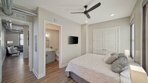 Een slaapkamer met een bed, een plafondventilator, een televisie en een deur naar een badkamer.