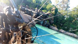 A bicycle wheel with a chain and gear mechanism, a rocky landscape, and a body of water.