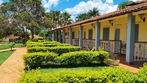 A courtyard with neatly trimmed hedges, a brick pathway, and a row of yellow buildings with green shutters.