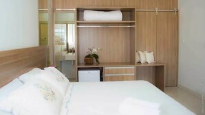 A hotel room with a bed, a wardrobe, a small desk, and a mirror.