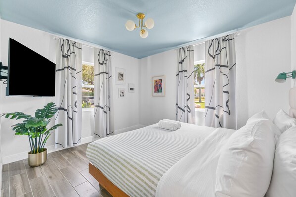 Un dormitorio con cama, cortinas, una planta y una lámpara de techo.